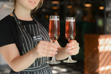 Beautiful young woman waiter serving two glasses of champagne in restaurant, cafe or bar. Bartender at work.