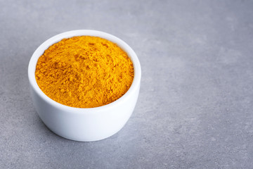 Bowl with turmeric powder on gray texture.