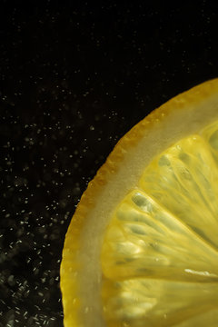 Juicy slice of lemon on a dark background. In the frame, only part of the citrus. Drops of water in the air. Detailed macro photo. Copyspace, minimalism.
