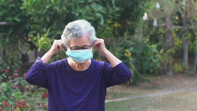 Elderly woman with short white hair wears face mask for healthy because have air pollution PM 2.5. Mask for protect Virus, Bacteria, Pollen Grains, Covid-19. Slow motion. Health care concept - Powered by Adobe