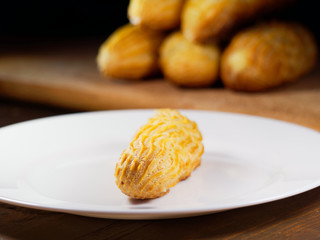 One eclair on a white plate, on a dark wooden background. Homemade baking.