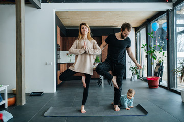 Infant child creeps next to his parents doing yoga