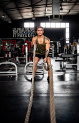 Fototapeta na wymiar Young attractive muscular generation z guy in crossfit gym using battle ropes