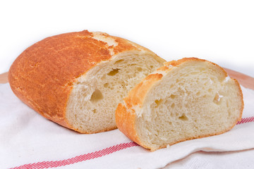 Partly sliced wheat bread on cloth napkin on white background
