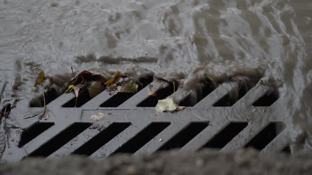 Rain water with debris flows down storm drain at the side of a street.