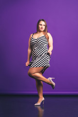 Sexy plus size fashion model in striped dress, attractive fat woman on purple background
