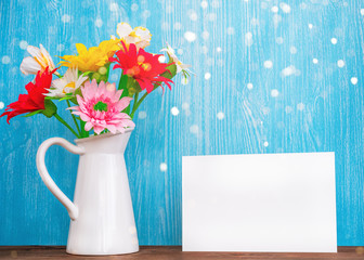 Vase with flowers and empty sheet of paper on a wooden background
