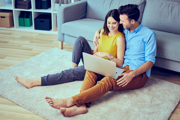 Couple using laptop sitting together at living room