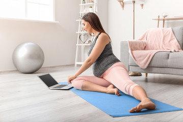 Beautiful sporty pregnant woman with laptop training at home