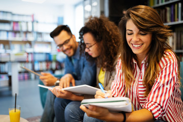 Group of happy students reading books and preparing to exam in library