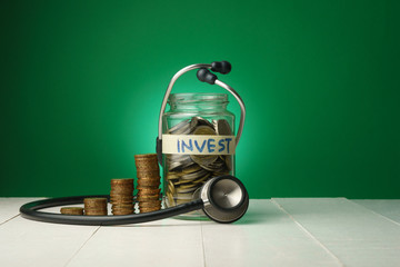 conceptual money growing, increasing finance situations, time cost money, finance checking. stacked money coins, a clock and a glass bottle of coins with a stethoscope againt green background
