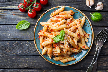 Penne pasta in tomato sauce and cheese decorated with basil on a wooden background, top view