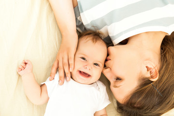 happy mother kissing a baby lying on a bed