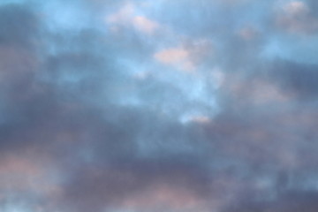 Dramatic blue sky with clouds backlit by the sun at dusk.
