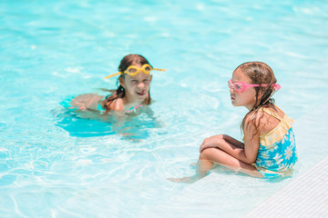 Adorable little girls playing in outdoor swimming pool on vacation