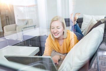Fototapeta premium Happy girl chatting online on laptop, window view. Smiling blonde woman messaging with friends on computer. Social media, communication and technology concept, copy space on wall