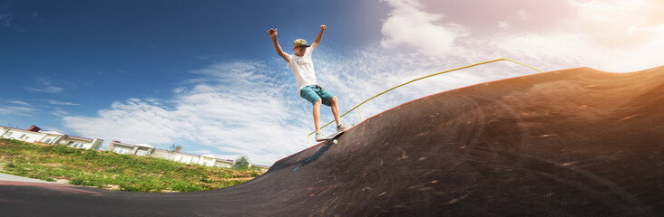 Portrait of a young skateboarder doing a trick on his skateboard on a halfpipe ramp in a skate park in the summer on a sunny day. The concept of youth culture of leisure and sports