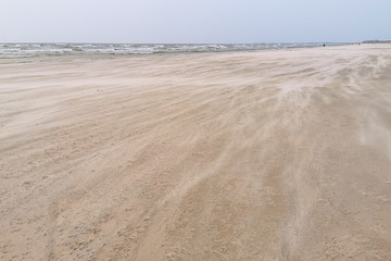 Strong wind drives waves of sand over deserted beach