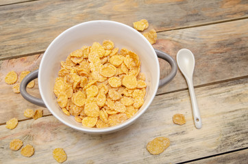 Bowl of cornflakes with a white spoon on a wooden background