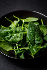 fresh spinach leaves in black plate on a dark background. top view