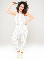 Portrait of beautiful smiling model with afro curls hairstyle dressed in summer hipster clothes.Sexy carefree girl posing in studio on gray background.Trendy funny and positive woman shows tongue