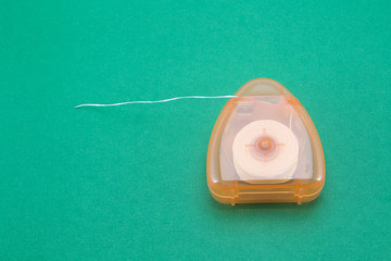 Dental floss in a transparent orange box on a green background close-up. The thread is pulled out...