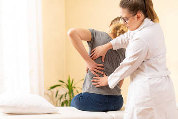 Female physiotherapist or a chiropractor examining patients back. Physiotherapy, rehabilitation concept. - obrazy, fototapety, plakaty