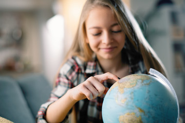 Portrait of cute little girl in living room looking globe. Pretty girl exploring world. 