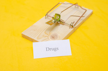 mousetrap with a piece of paper and the words Drugs on a yellow background. concept of drug. copy space