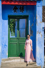 Young Asian woman wearing Vietnamese traditional dress standing at the green door.