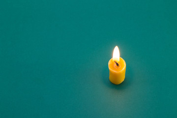A small short orange candle without a candlestick burns on a green table (background). The candle...