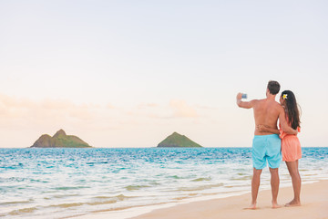 Beach vacation tourists couple taking picture with phone of Hawaii islands. Honeymoon summer travel...
