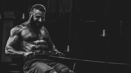 Fototapeta na wymiar Young strong bearded bodybuilder doing low cable pulley row seated, dramatic black and white image