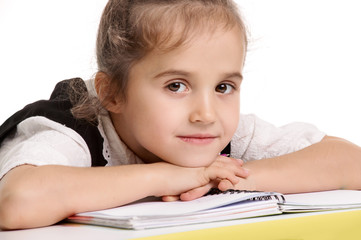 Portrait of cute smiling girl lying on school desk after lesson