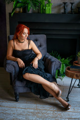 a beautiful red-haired woman in a black dress is sitting in a chair