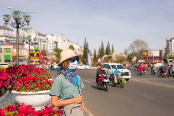 Caucasian woman wearing sanitary mask outdoors in Da Lat city centre Vietnam. Tourist with medical mask protection against risk of chinese flu virus epidemy in Asia. Anti smog mask traffic pollution.