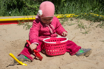 Child of two years old playing with sand and shovel in sandbox on the playground