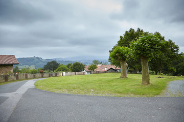 Village, rural landscape at cloudy summer  day, farm buildings with tiled roofs. Road, house and fence, countryside, Atlantic Pyrenees, France. Overcast weather