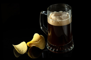Beer in a transparent glass and potato chips on a black glass background