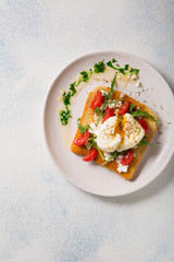 French breakfast concept. Poached egg on toasted bread with cherry tomatoes, cheese and herbs on a boiled background