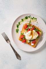 French breakfast concept. Poached egg on toasted bread with cherry tomatoes, cheese and herbs on a boiled background