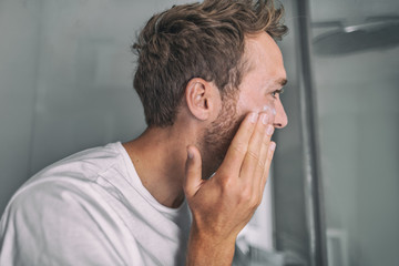 Skin care young man putting face cream for facial acne treatment in home bathroom. Men beauty skincare lifestyle.