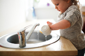 Toddler child washes dishes in sink