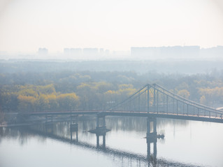 Naklejka premium Hazy morning view on pedestrian Park Bridge, Trukhaniv island and left riverside of Dnieper river in Kyiv, Ukraine