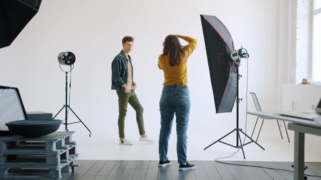 Female photographer is showing body positions to male model working in studio together taking pictures for fashion advertisements. Youth and advertising concept.