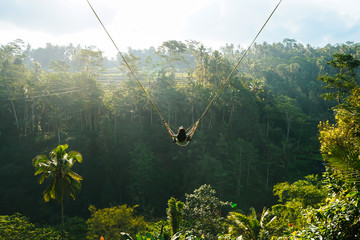 Back view of woman while swing with natural forest background in sunlight, travel and amazing...