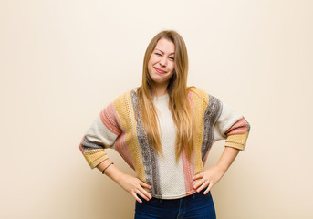 young blonde woman looking happy and friendly, smiling and winking an eye at you with a positive...