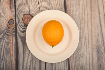 Ripe yellow lemon on a white plate on a wooden background. Close up.