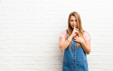 young blonde woman looking serious and cross with finger pressed to lips demanding silence or...