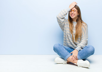 young blonde woman raising palm to forehead thinking oops, after making a stupid mistake or...